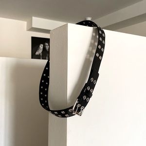 Black faux leather belt with silver tone grommet pattern.